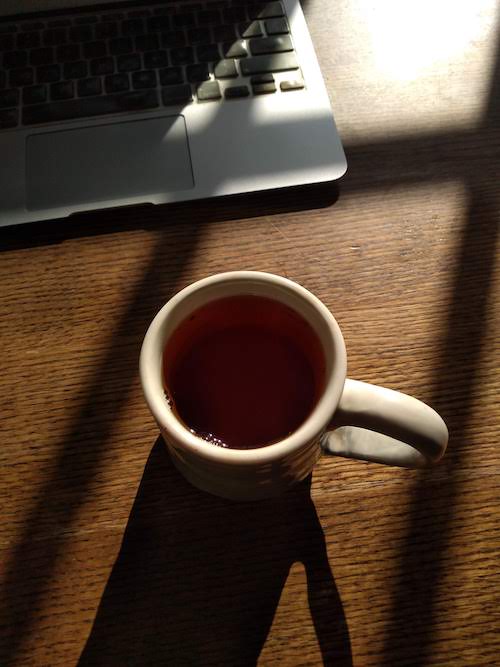 A photo of a cup of tea on a wooden table, a laptop computer in the background. 